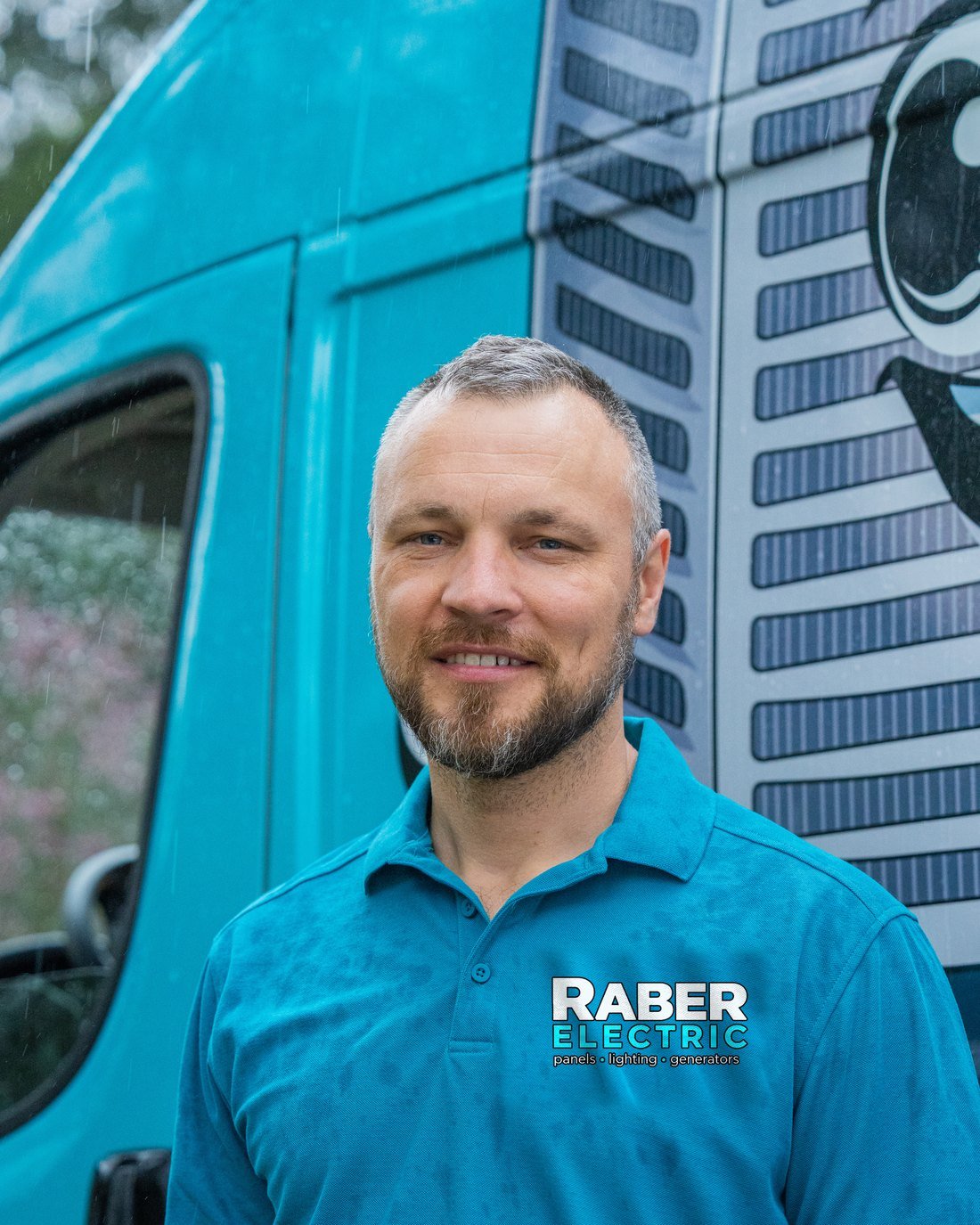 Raber Electric technician in a branded polo beside a service van