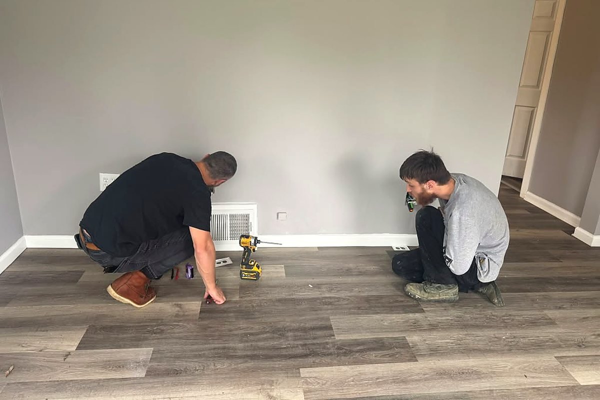 Two Raber Electric electricians replacing receptacles along a baseboard in a finished room