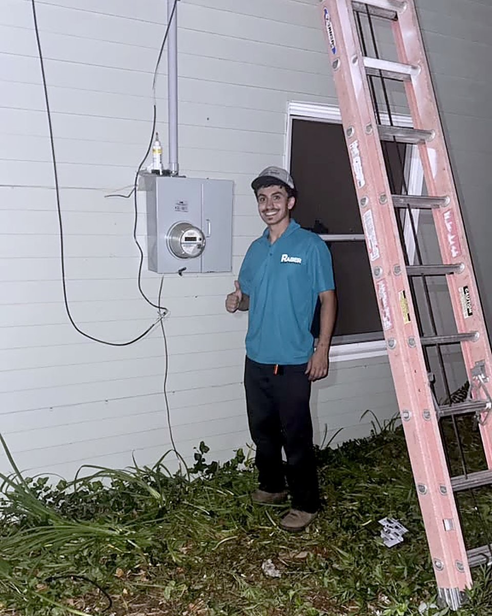 Raber Electric technician beside a newly installed meter socket and service panel on a home